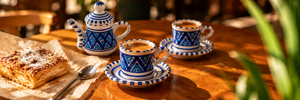 Service Sidi Bou Saïd avec théière, deux tasses de café et une pâtisserie sur une table en bois au soleil.