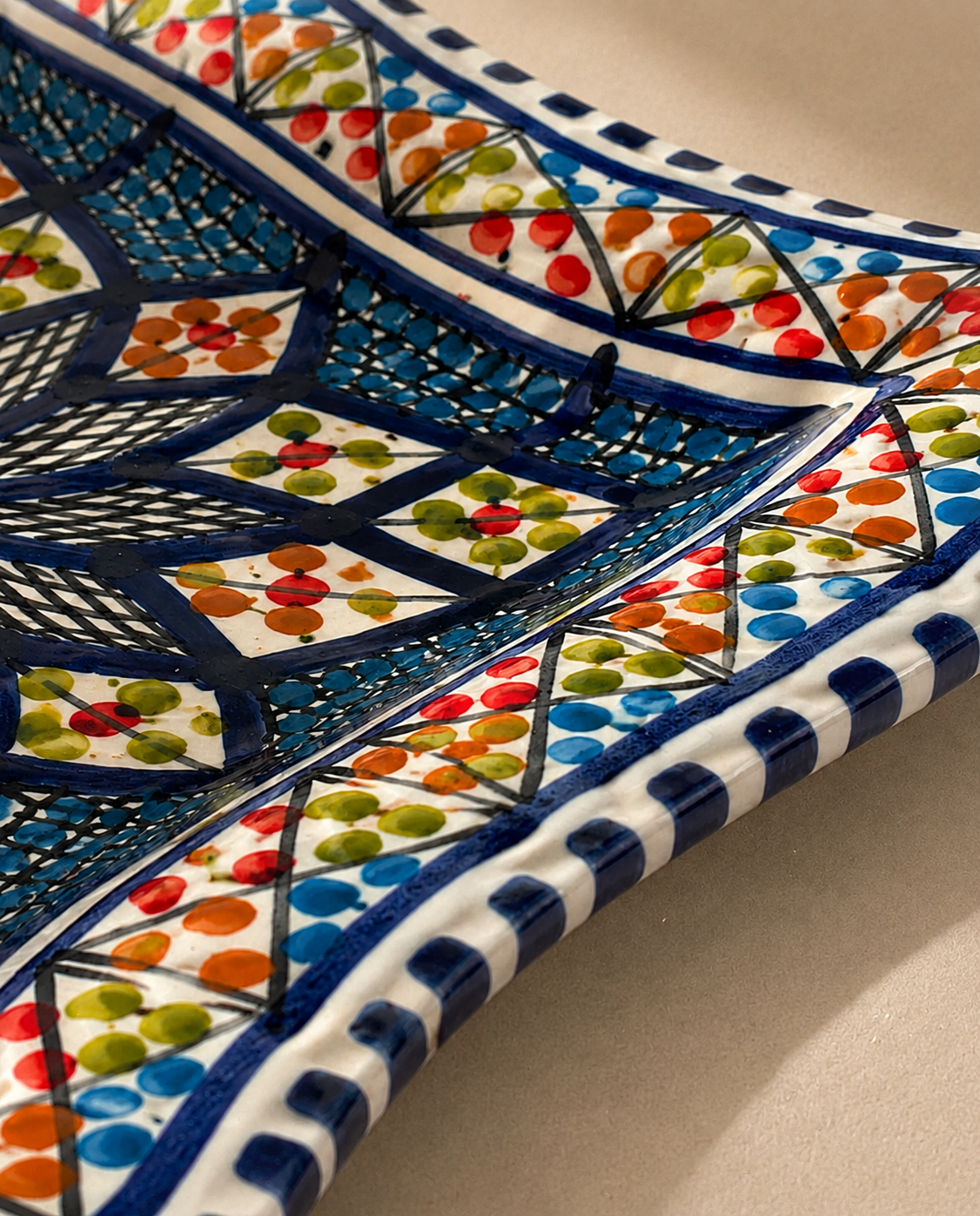 Gros plan sur les motifs d'une assiette carrée en céramique artisanale tunisienne de la collection Médina.