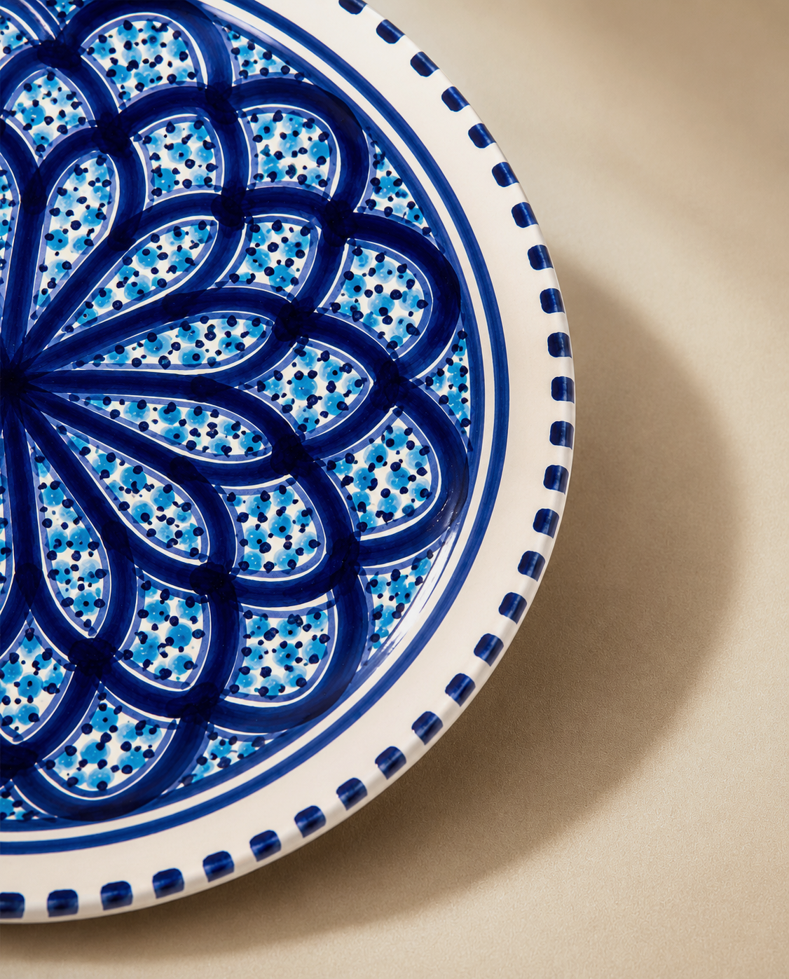 Gros plan sur les motifs peints à la main d'une assiette plate en céramique artisanale tunisienne de la collection Sidi Bou Saïd.